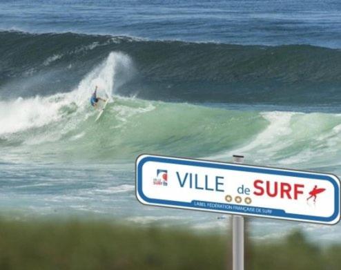 a sign at the beach with a surfer riding a wave at T3 - TERRASSE 30 m2 VUE OCEAN, 2 CHAMBRES, parking privatif et piscine en été in Lacanau-Océan