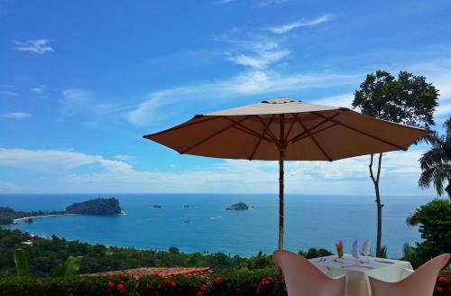 a table with an umbrella and a view of the ocean at Hotel La Mariposa in Manuel Antonio