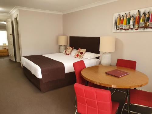 1 dormitorio con 1 cama y 1 mesa con sillas rojas en The Aston Motel Tamworth, en Tamworth