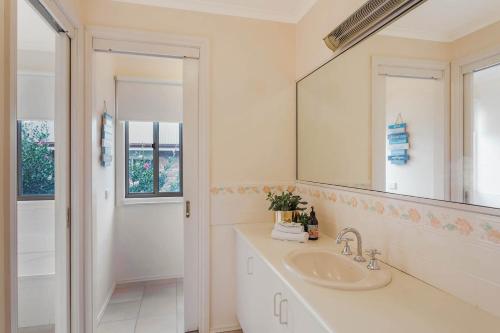 a white bathroom with a sink and a mirror at Pelican Lake Holiday House in Merimbula