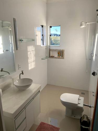 une salle de bain blanche avec un lavabo et des toilettes dans l'établissement Casa com piscina fundo pra represa e AR Condicionado CasinhaBrancaDeVaranda, à Ijaci