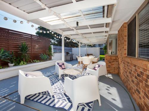 a patio with white chairs and a brick wall at Meeseeks I Pet Friendly I 2 Mins Walk to Beach in Culburra Beach