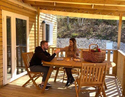 un homme et une femme assis à une table en bois sur une terrasse couverte dans l'établissement Les Cottages du Herisson, à Bonlieu