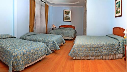 three beds in a room with blue walls and wooden floors at Hotel Yanuncay in Cuenca