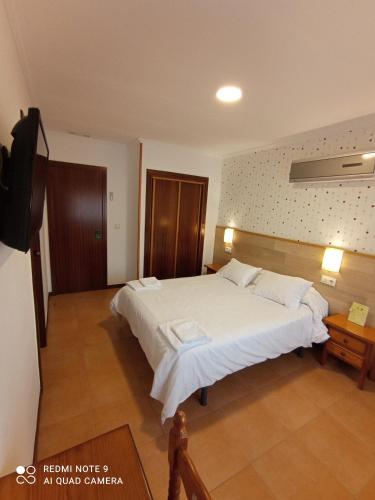 a bedroom with a large white bed and a television at Pensión O Escondidino in Baiona