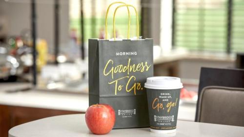 a bag and an apple on a table with a cup of coffee at Staybridge Suites - Waterloo - St. Jacobs Area in Waterloo