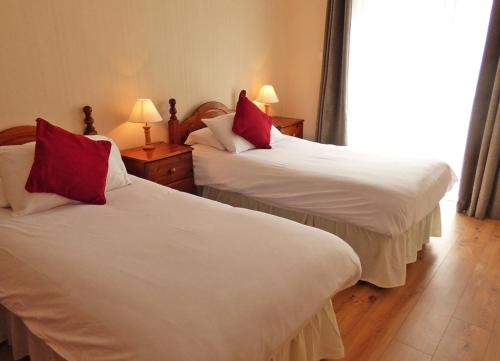 two beds with red pillows in a hotel room at Kilkee Holiday Homes Ground Floor in Kilkee