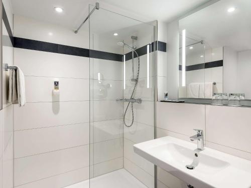a white bathroom with a shower and a sink at Mercure Hotel Bielefeld Johannisberg in Bielefeld