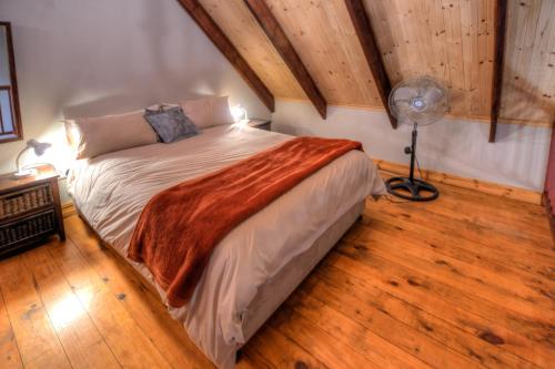 a bedroom with a bed and a fan and wood floors at Laragh-on-Hogsback in Hogsback