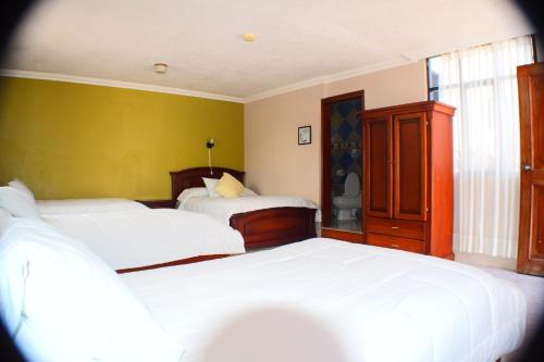 a bedroom with two beds and a yellow wall at Hosteria Casa Giralda in Baños