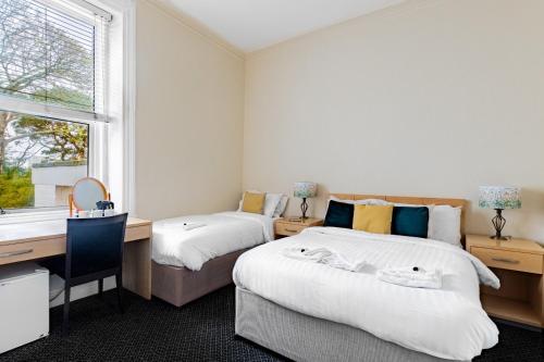 two beds in a room with a desk and a window at Brooklands Lodge in Bournemouth