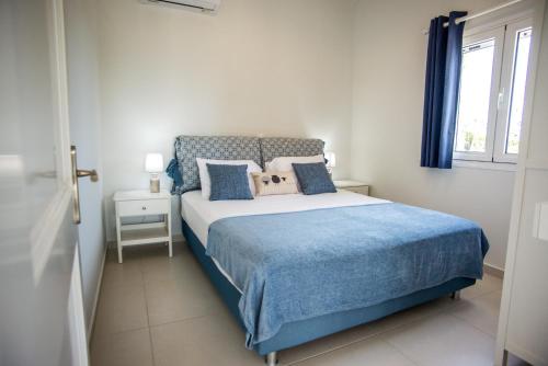 Schlafzimmer mit einem Bett mit blauer Bettwäsche und einem Fenster in der Unterkunft Xarafailte Summer House in Metaxáta