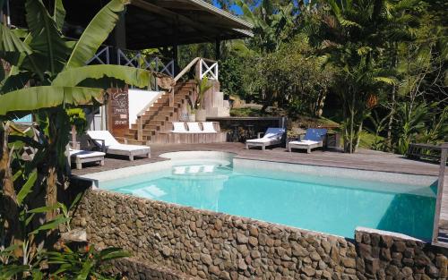 a swimming pool with a stone wall and chairs and a staircase at Finca Vela Lodge in Bocas Town