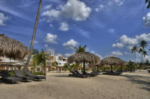 a beach with chairs and straw umbrellas and palm trees at Appartamenti in Cadaques Caribe in Bayahibe