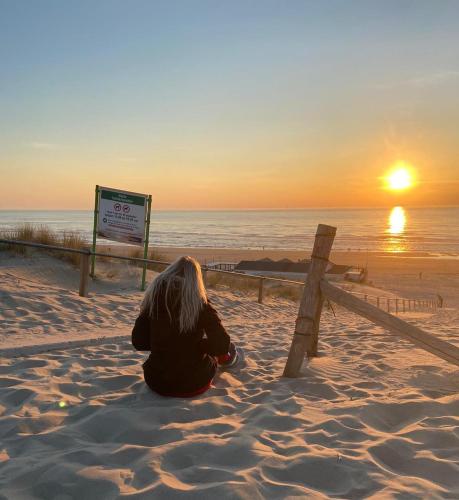 a woman sitting on the beach watching the sunset at Heerlijke vakantiehuizen in Egmond in Egmond aan Zee