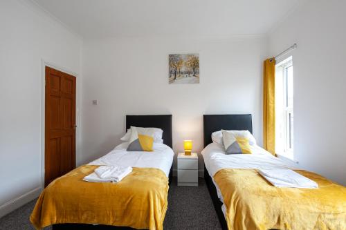 2 camas en una habitación con paredes blancas y sábanas amarillas en Inspired Stays-City Centre Location- Sleeps up to 9, en Stoke on Trent