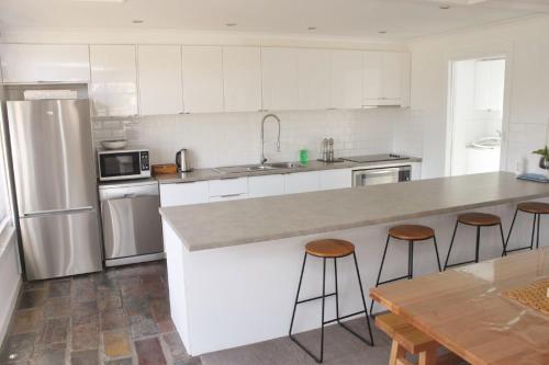 a kitchen with white cabinets and a counter with stools at Elusive Penguin in Bicheno