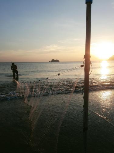 mężczyzna stojący na plaży z siecią rybacką w obiekcie บ้านสุขกมลแววดาวบ้านเดี่ยว1ห้องนอน w mieście Ban Pak Nam