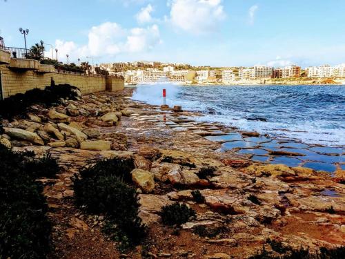 a beach with rocks and the water and buildings at Aurora in Marsaskala