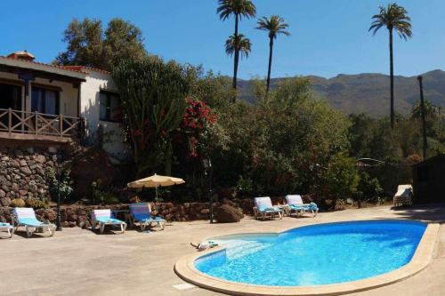 a swimming pool with chairs and a house and palm trees at Casa rural EL Olivar - El Orujo in Santa Lucía