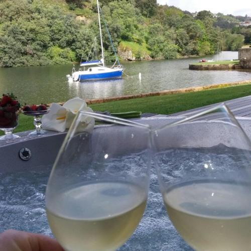 two glasses of white wine with a boat in the water at Douro Suites in Riba Douro