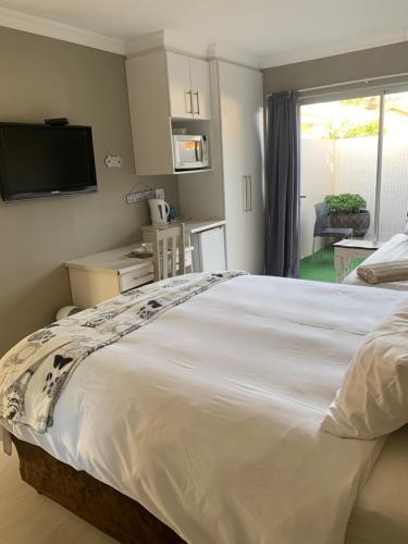 een slaapkamer met een groot wit bed en een televisie bij Sharwood Place in Port Elizabeth