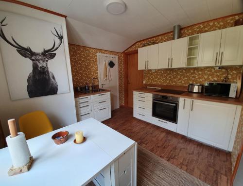 a kitchen with white cabinets and a deer picture on the wall at Ferienwohnung Lövåsängen im Waldbauernhof, Årjäng in Årjäng