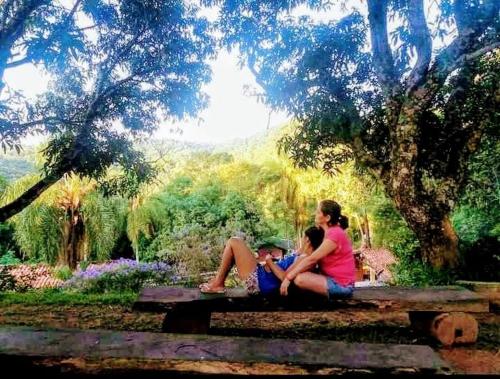 two women sitting on a bench in a park at Sitio Arco Iris da Lia in São Roque