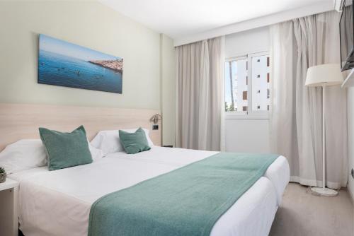 a hotel room with a large white bed and a window at Olive Beach Apartamentos in Port d'Alcudia