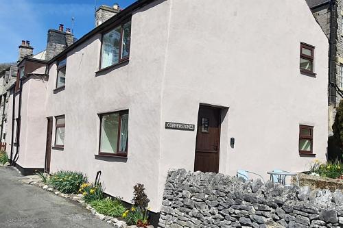 a white building with a stone wall and a door at Cornerstones Cottage, Tideswell in Tideswell