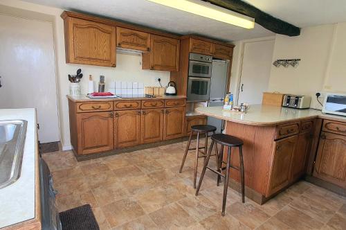 a kitchen with wooden cabinets and bar stools at Cornerstones Cottage, Tideswell in Tideswell