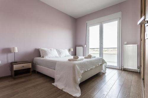 a white bedroom with a bed and a large window at Μodern apartment with big garden in Epanomi