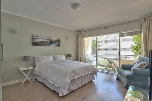 a bedroom with a bed and a chair and a window at Clifton 1st Beach Studio in Cape Town