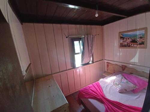 a small pink room with a bed and a window at Casa de Campo da Vó in Urupema