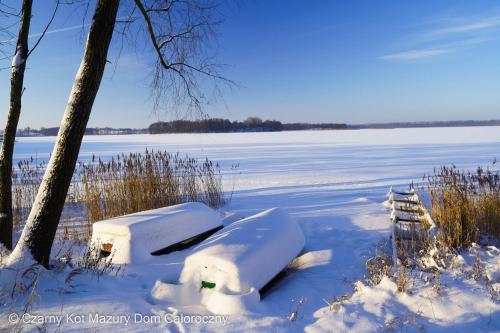 a boat is covered in snow next to a tree at Czarny Kot Mazury Dom Całoroczny in Małkinie