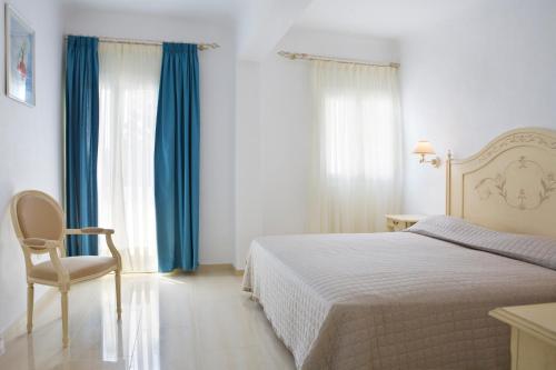 a bedroom with a bed and a chair and blue curtains at Kamari Hotel in Platis Yialos Mykonos