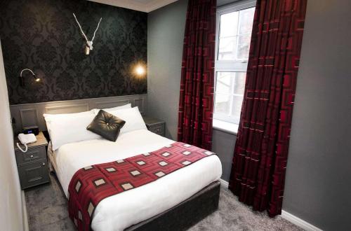 a bedroom with a bed with red curtains and a window at St James Hotel; BW Premier Collection in Nottingham