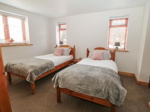 two beds in a room with two windows at Farm Yard Cottage in Pickering