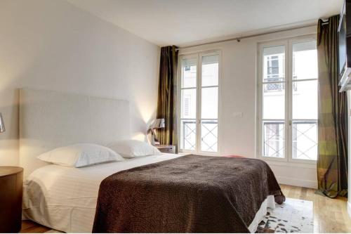 a bedroom with a bed with white sheets and windows at Appartement Champs-Elysées Montaigne - HALA PARIS in Paris