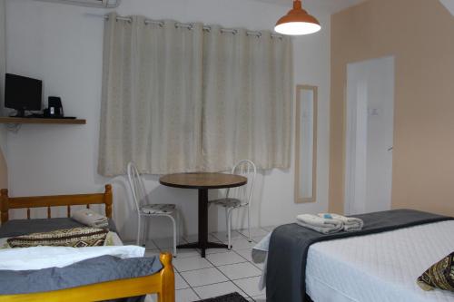 a room with two beds and a table and a window at Pousada Flay 7 minutos Próximo do Aeroporto de Florianópolis in Florianópolis