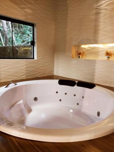 uma grande banheira branca numa casa de banho com uma janela em Pousada Bosque em Monte Verde