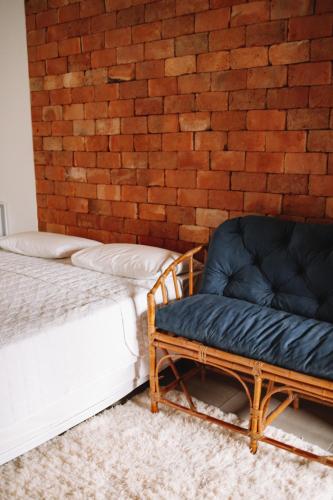 a bed and a chair next to a brick wall at Sapê Guest Hotel in Praia do Rosa