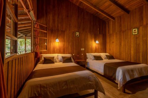 two beds in a room with wooden walls at El Jardín Hotel & Restaurante in Puyo