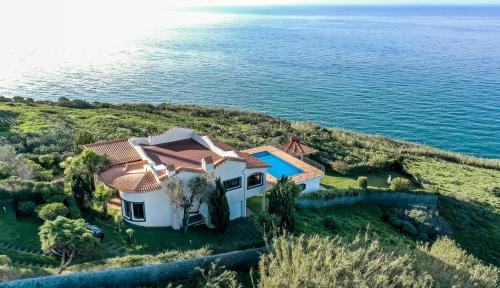 een luchtzicht op een huis op een heuvel naast het water bij Secluded Sunset Villa on Cliff & 180 Degree Ocean Views in Fajã da Ovelha