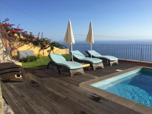 una terraza con piscina, sillas y sombrillas en Villa Pargo, en Fajã da Ovelha