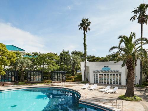 a pool with chairs and palm trees in front of a building at Bloom Hotel in Seogwipo