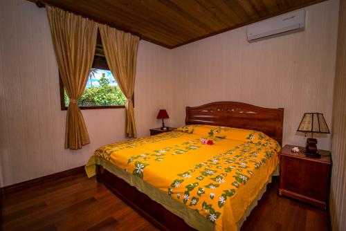 a bedroom with a bed with a yellow comforter and a window at Moorea Golf Lodge in Maharepa