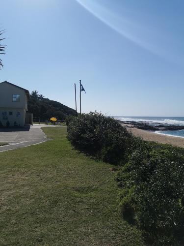a park next to the beach with a building and the ocean at Aloe Self Catering in Port Shepstone