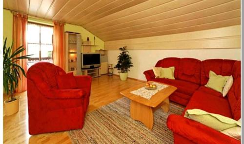 sala de estar con sofá rojo y mesa en Haus Brigitte im Dreiländereck en Neureichenau