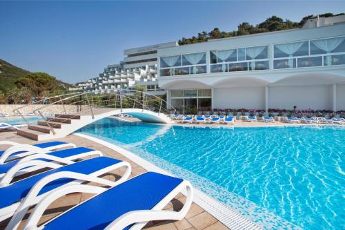 una piscina con sillas azules y blancas y un edificio en Hotel Narcis - Maslinica Hotels & Resorts, en Rabac